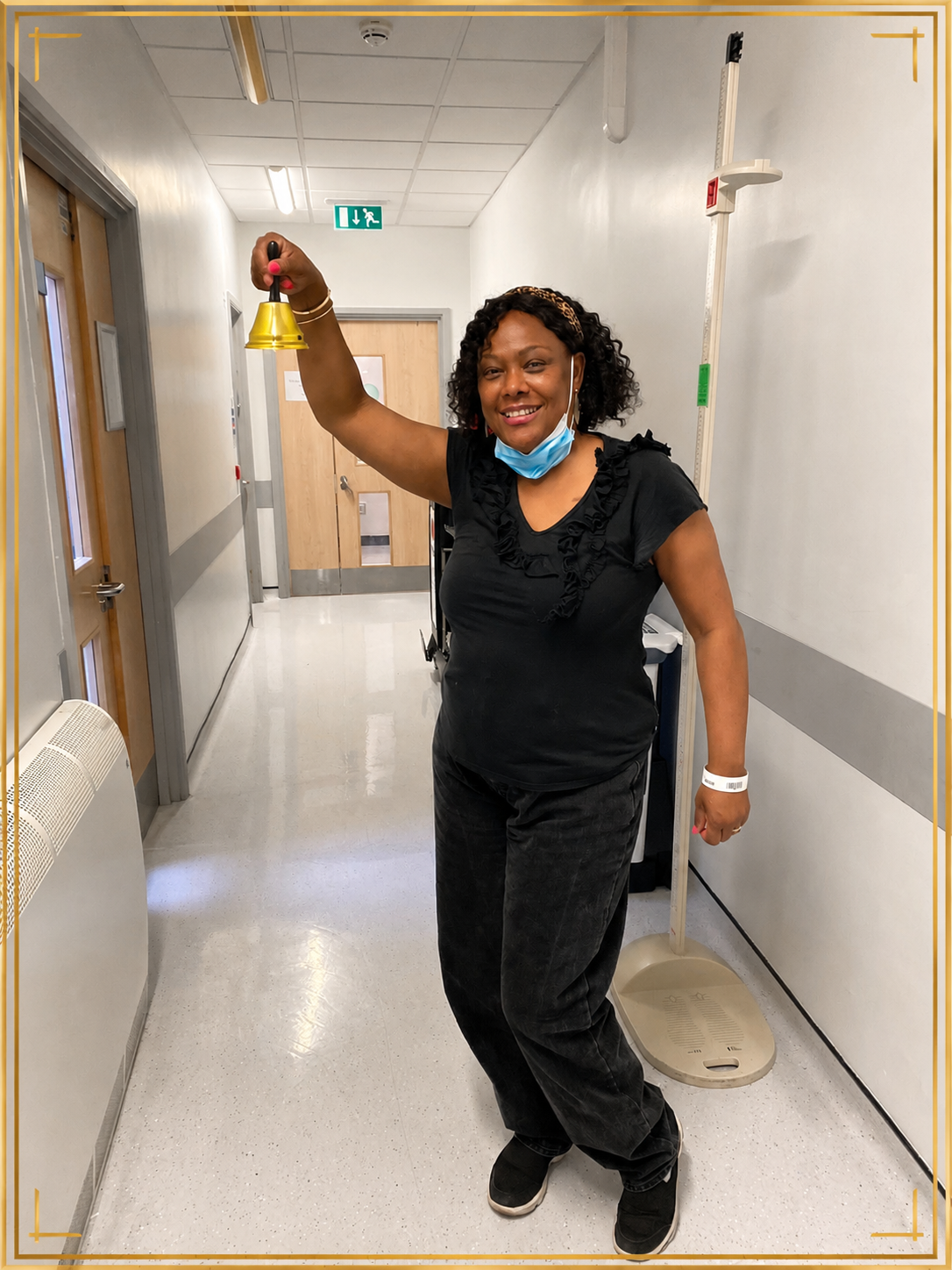 Sharon-Ann Phillips ringing a gold bell in a hospital corridor — celebrating a milestone in her cancer treatment