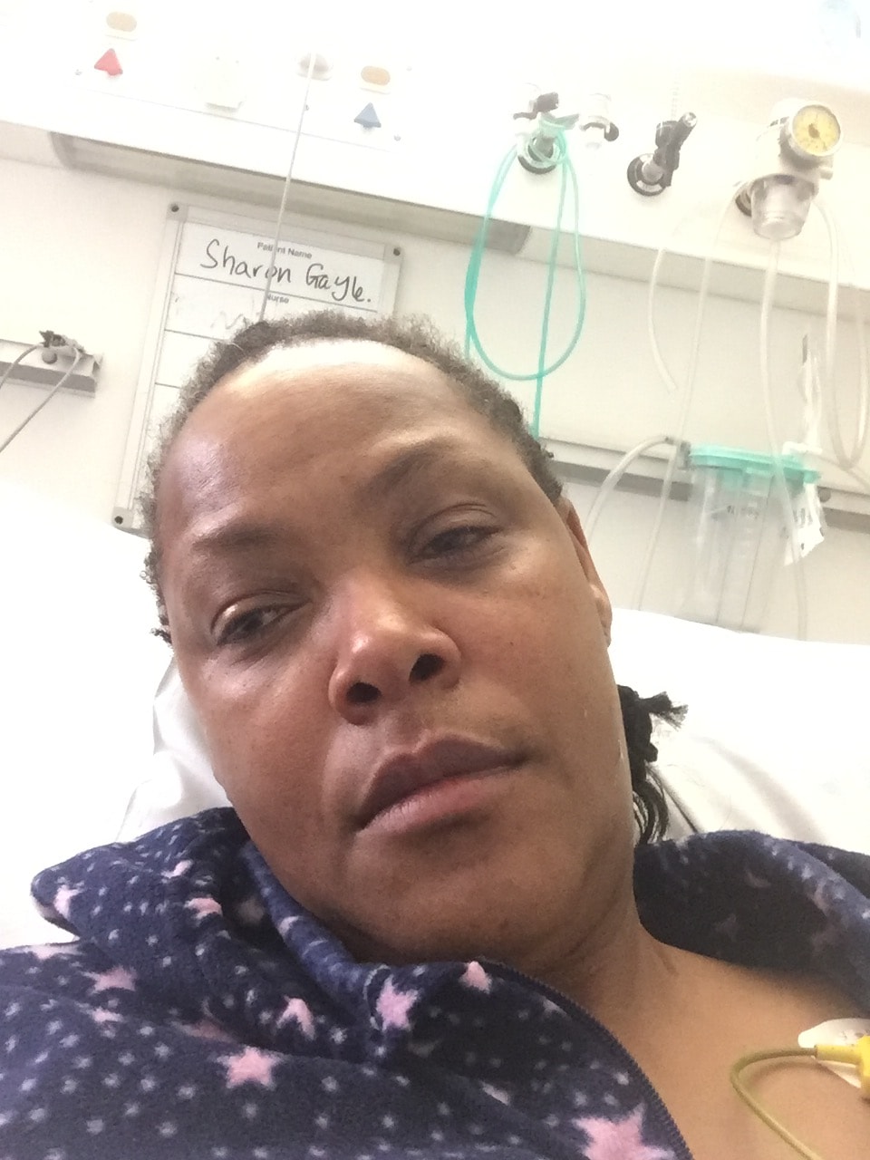 Sharon-Ann Phillips in a hospital bed during cancer treatment — a powerful image of resilience