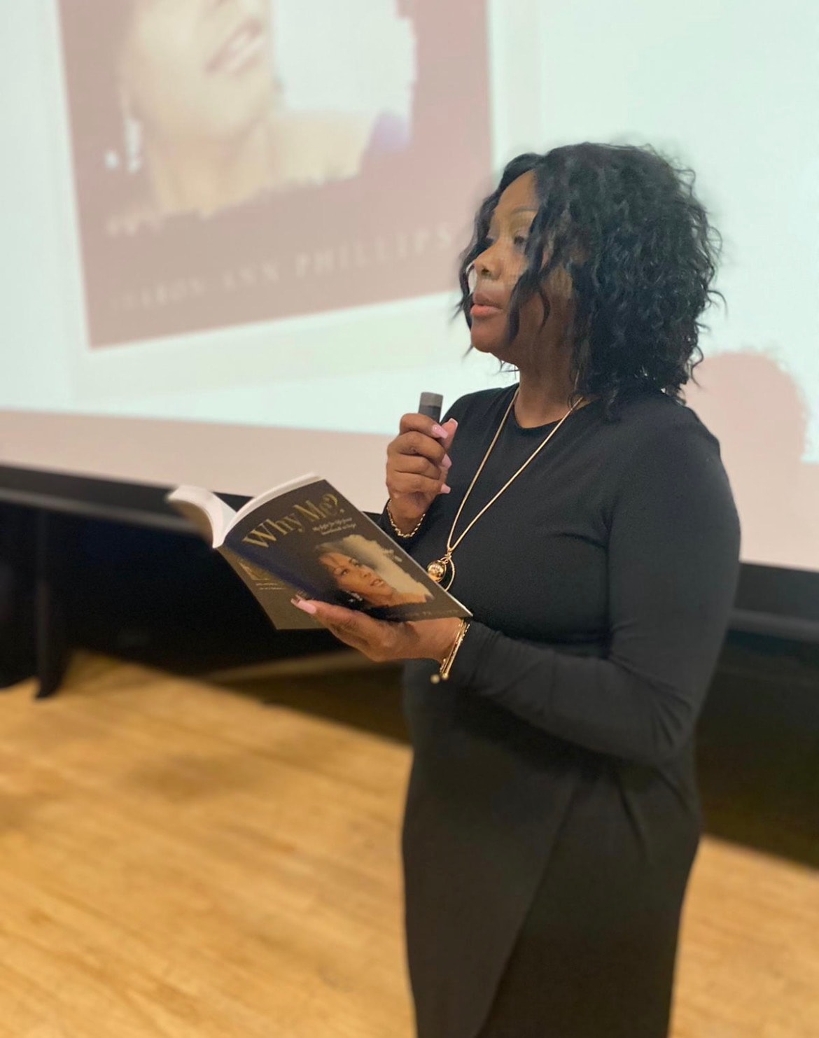 Sharon-Ann Phillips speaking at a church podium holding her book Why Me?